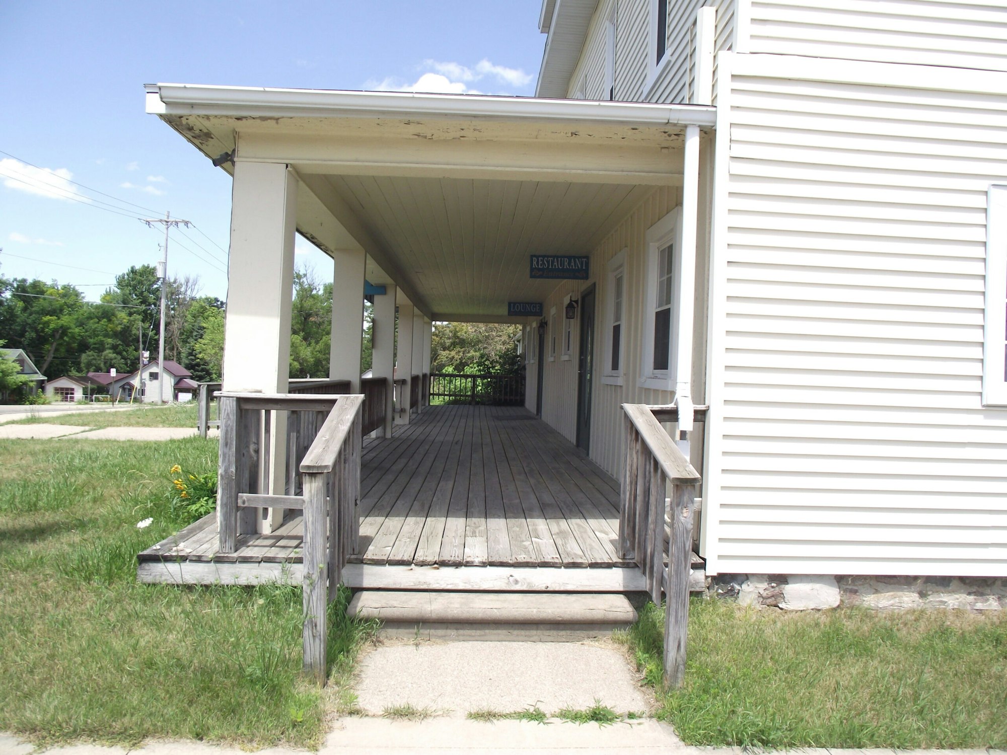 A wooden porch with railing leads to a beige building labeled "Restaurant" and "Lounge" signs.