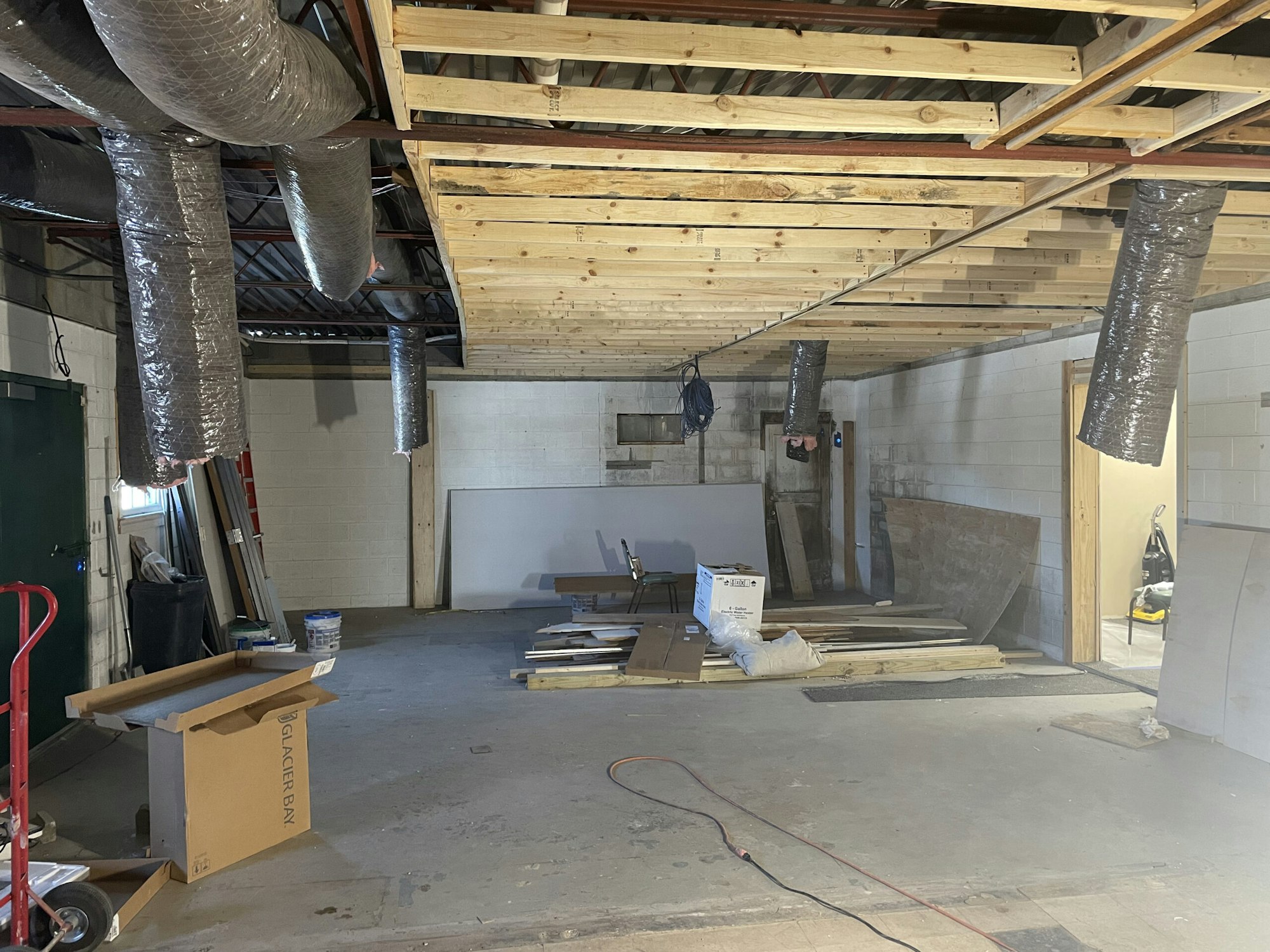 A room under construction with exposed ductwork, wooden beams, insulation, and construction materials scattered around.