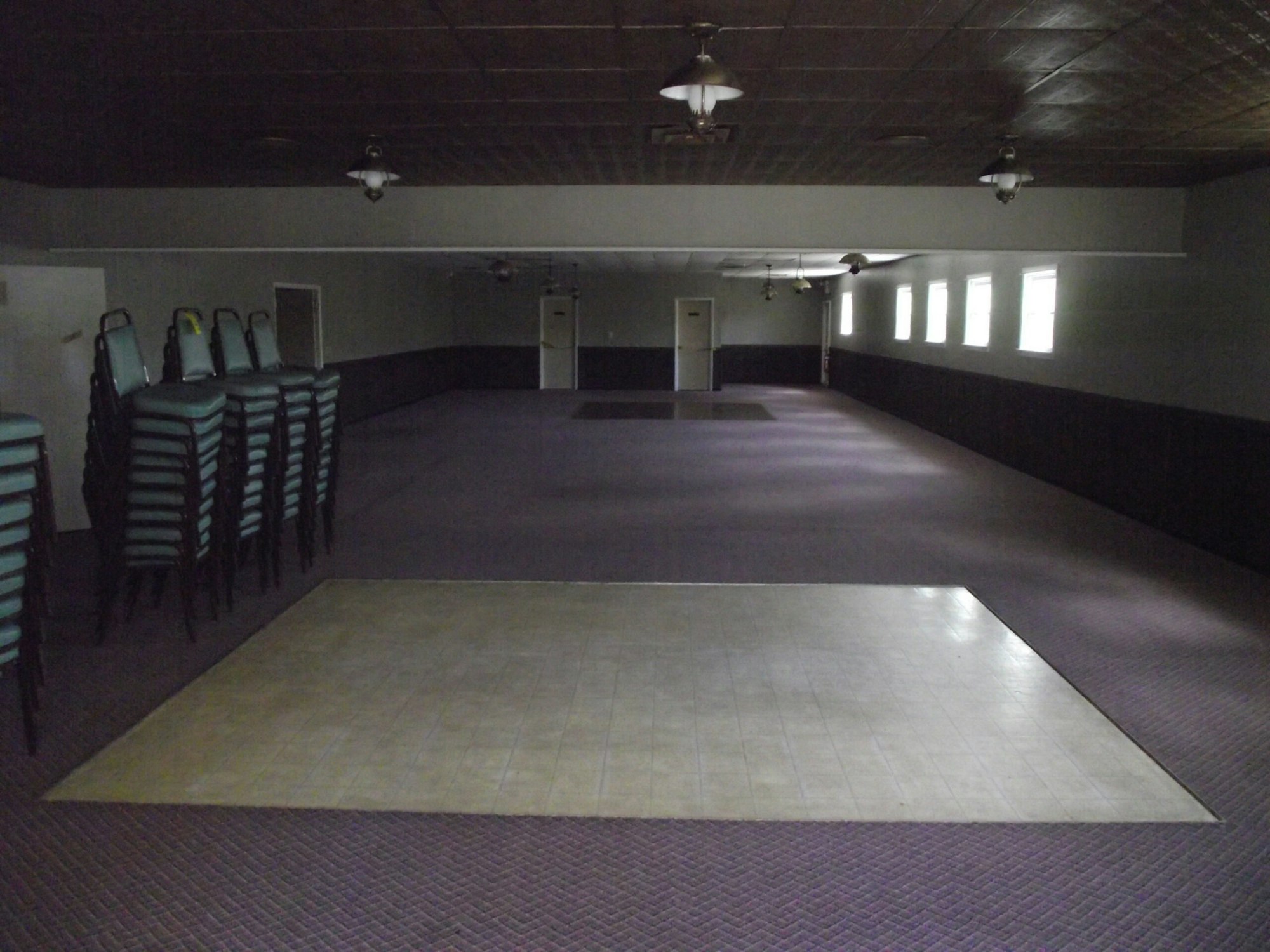 Empty hall with stacked chairs on the left and a dance floor in the center.
