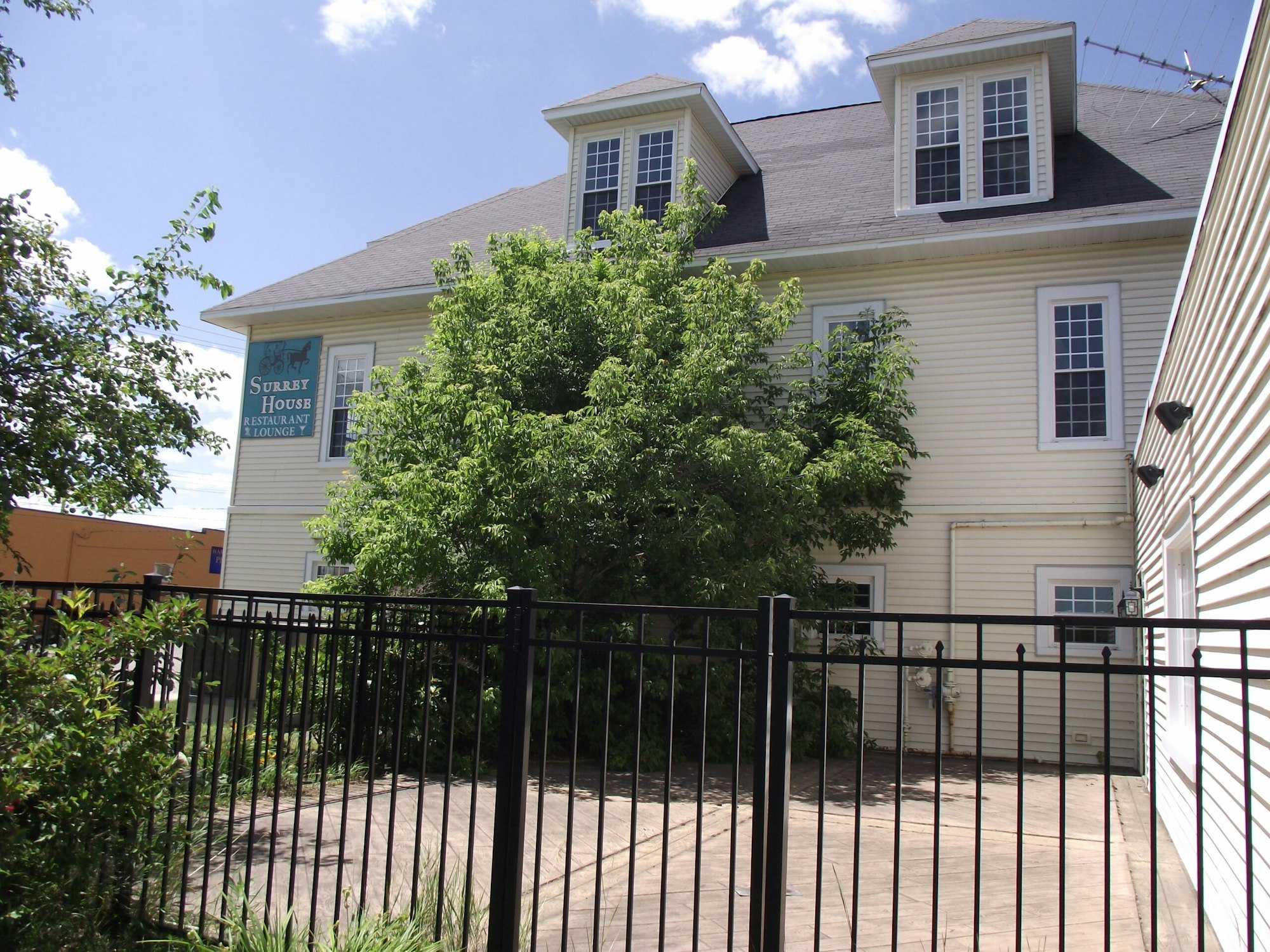 A two-story building labeled "Surrey House Restaurant & Lounge" with trees and a black fence in front.