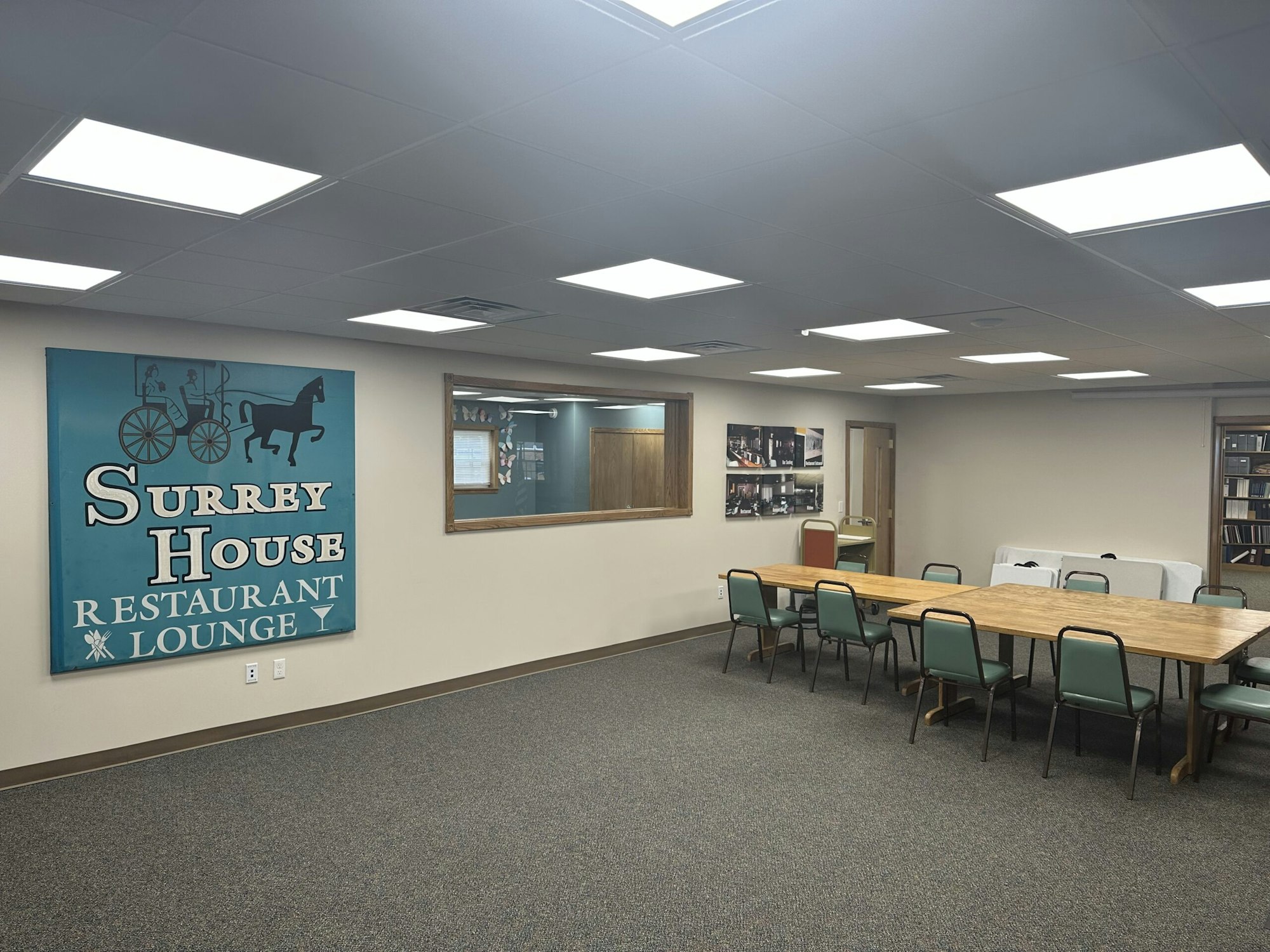 Room with a long table, chairs, a "Surrey House Restaurant Lounge" sign, and framed photos on the walls.