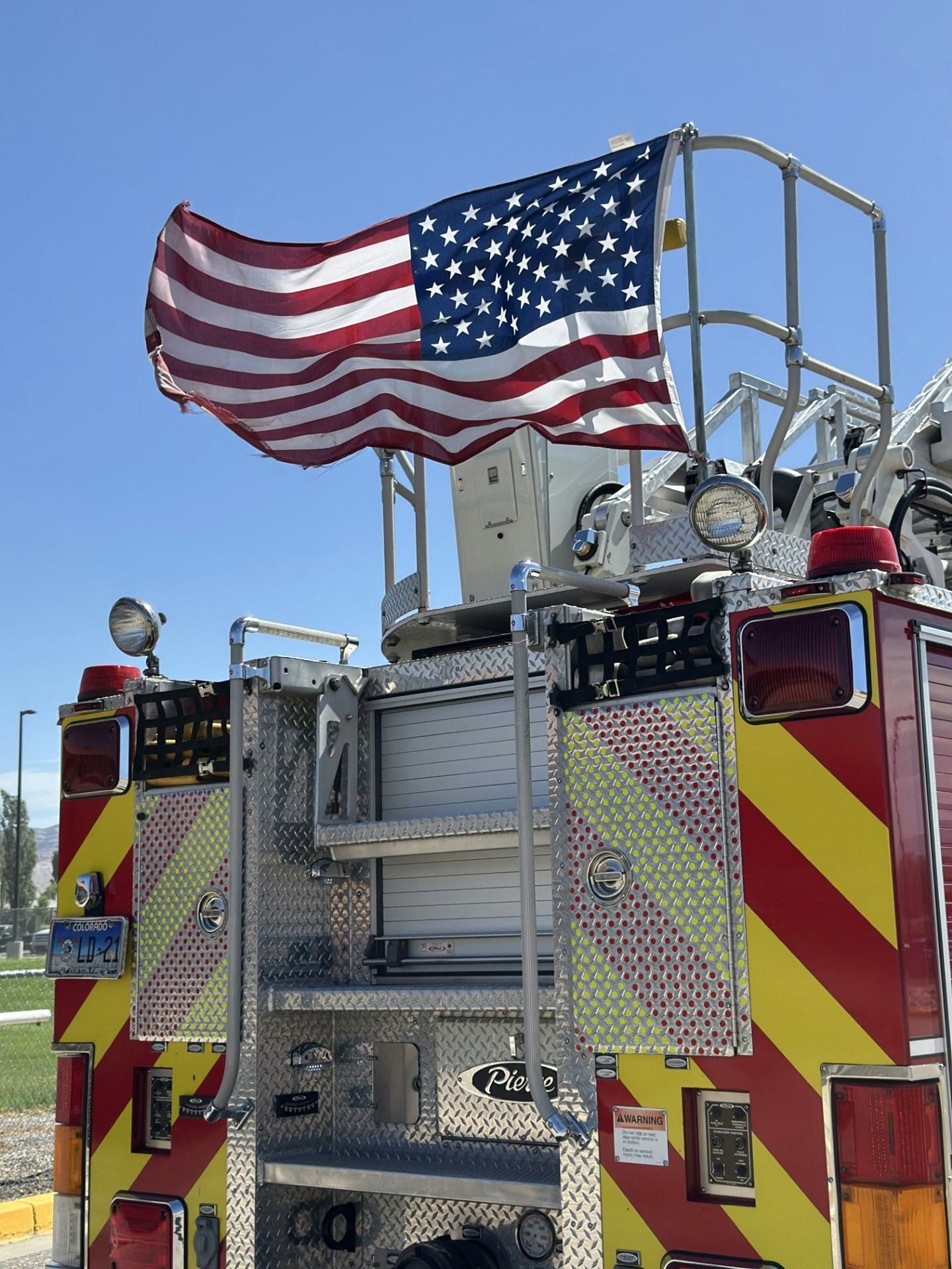 A fire truck with an American flag attached, set against a clear blue sky.