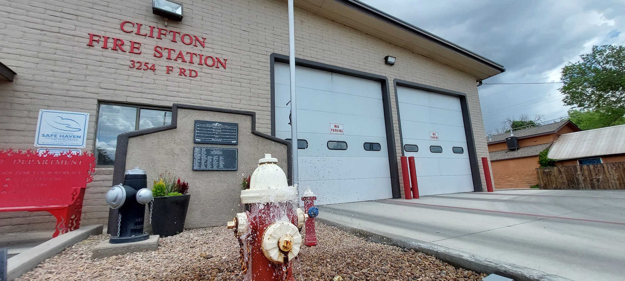 Fire station with two garage doors, hydrants, and "Safe Haven for Newborns" sign in front.