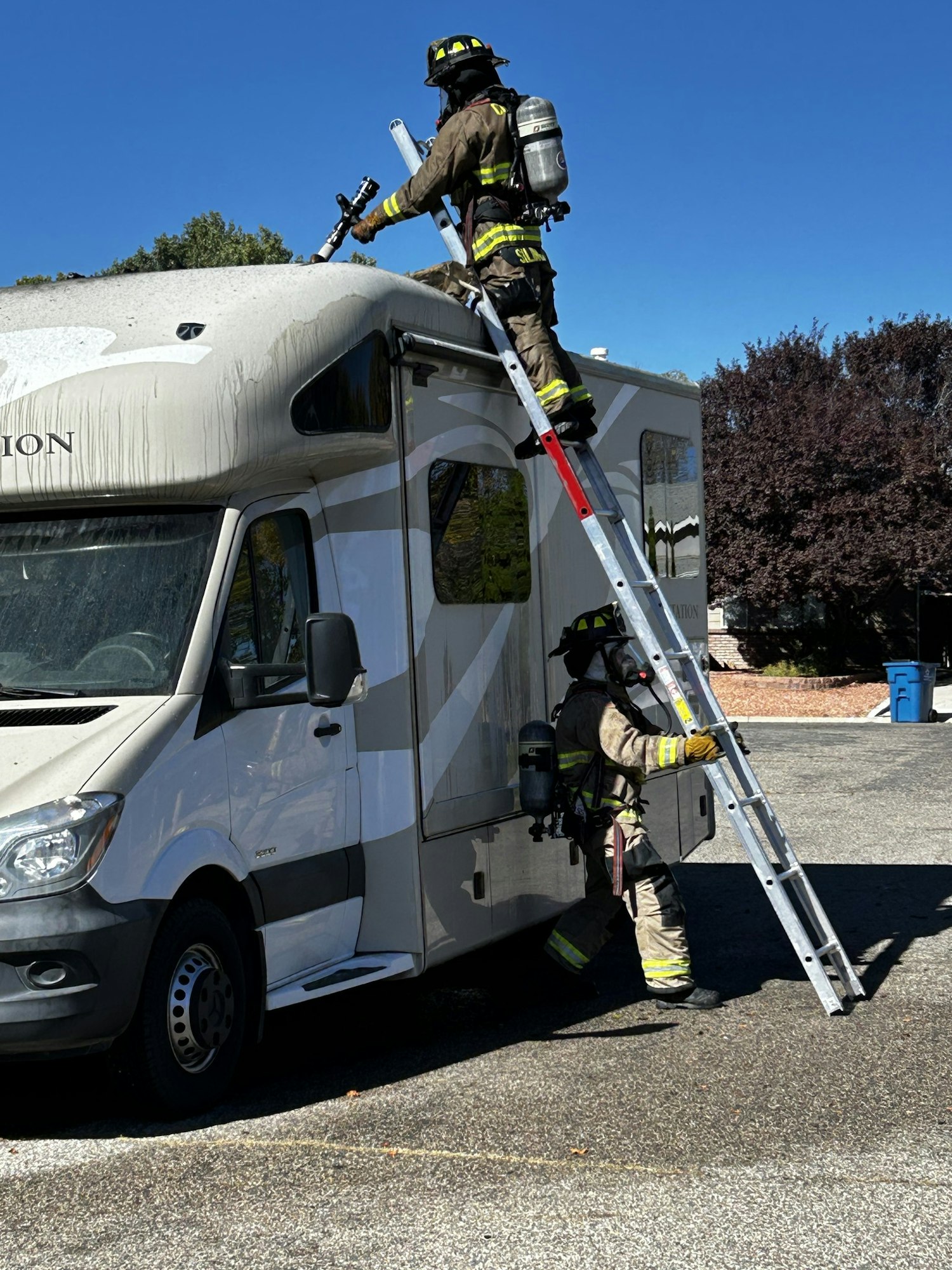 Two firefighters on a ladder dealing with a situation on top of an RV.