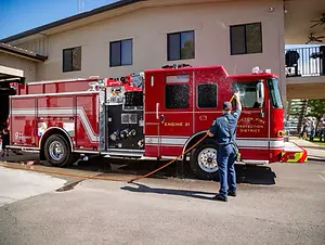 A person is washing a red fire truck with a hose in front of a building.