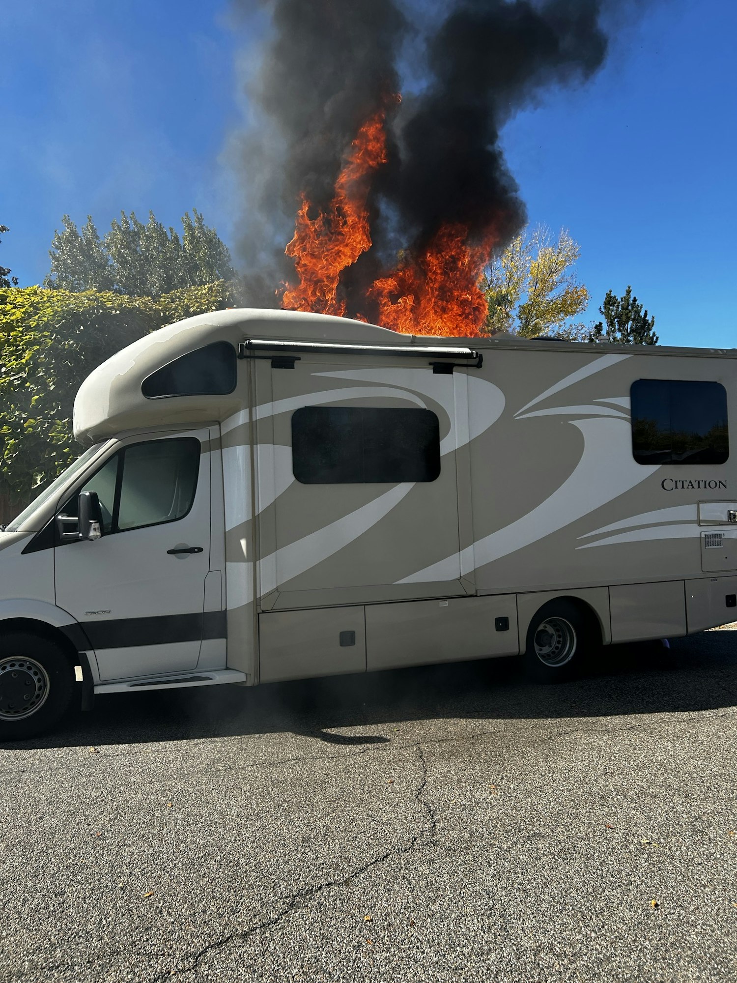 An RV is on fire with large flames and black smoke rising from its roof.