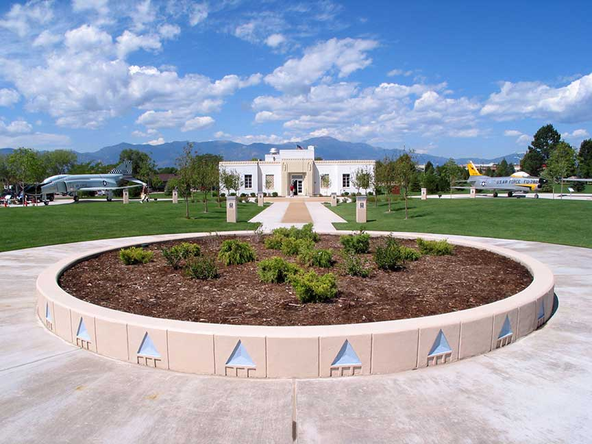 Circular garden in front of a building with airplanes on display and mountains in the background.
