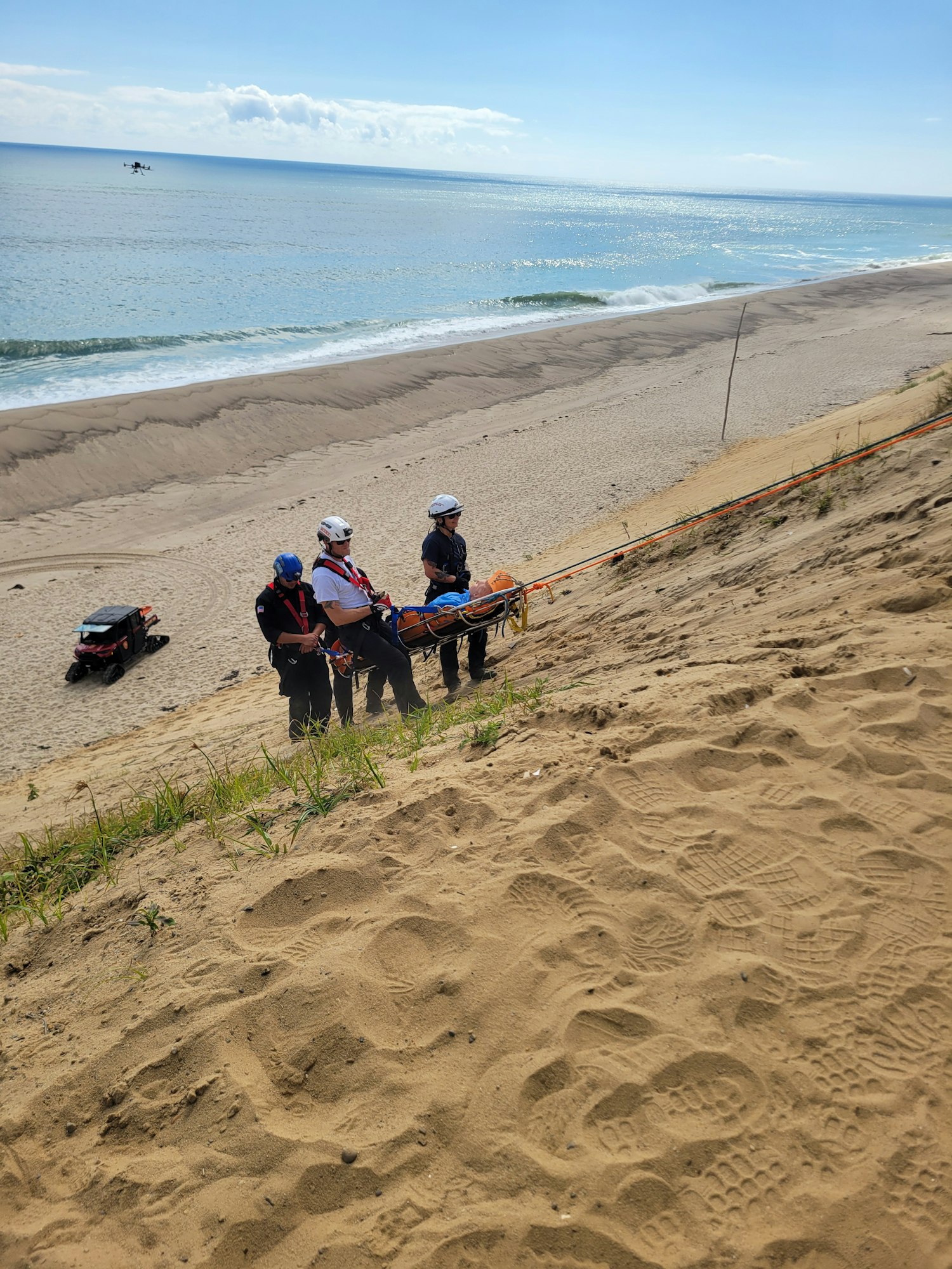 People with gear standing on a sandy cliff near the ocean.