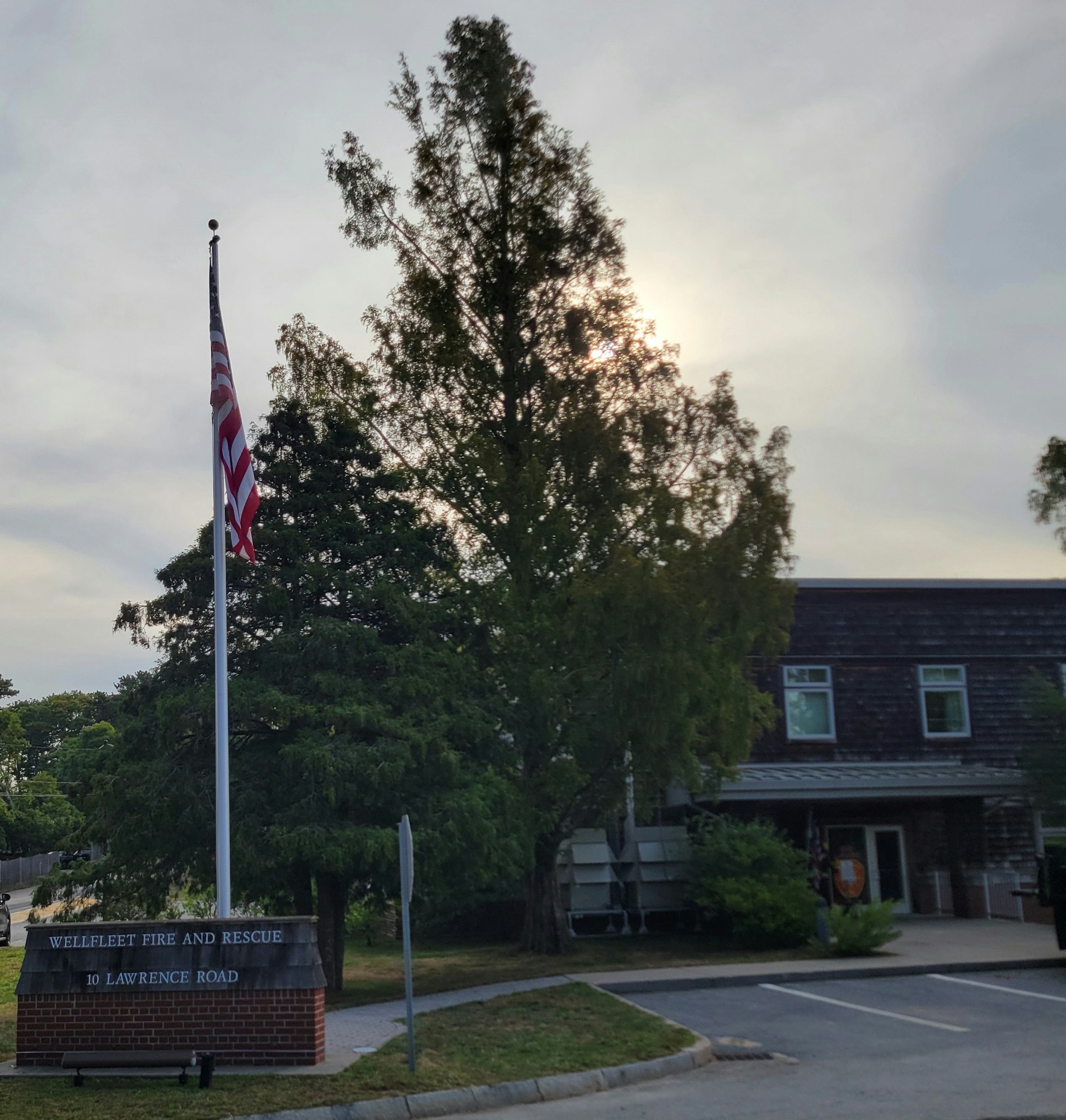 Wellfleet Fire and Rescue sign, U.S. flag, trees, and a building in the background.