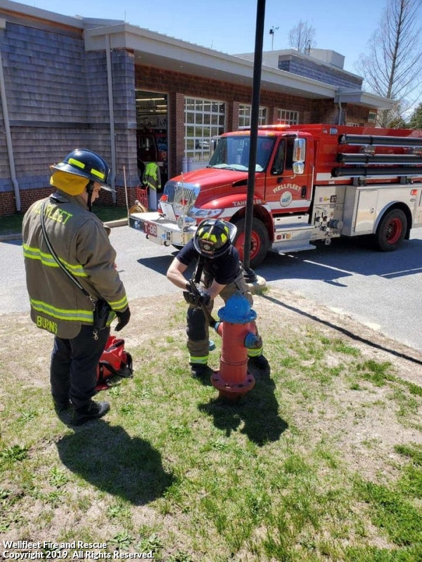 Firefighters checking a hydrant with a fire truck in the background.