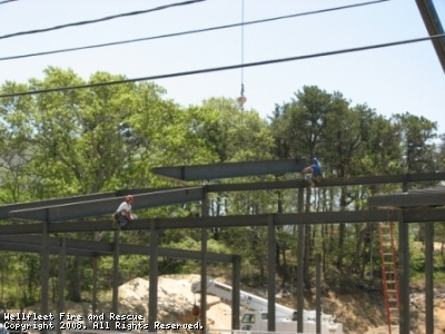 Construction workers on steel beams of a building under construction with trees in the background.