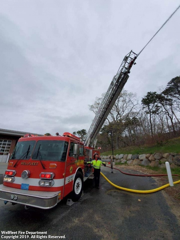 A firefighter with a fire engine and extended ladder under a cloudy sky.