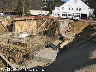 Construction site with foundation work, rebar framework, and a worker near a building.