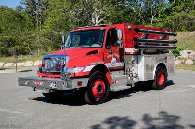 A red fire truck equipped with hoses and emergency lights, parked outdoors.