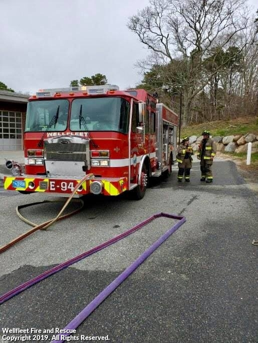 A red fire engine with firefighters in gear standing beside it.