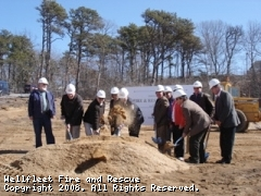 Group of people with hard hats using shovels at a groundbreaking ceremony.