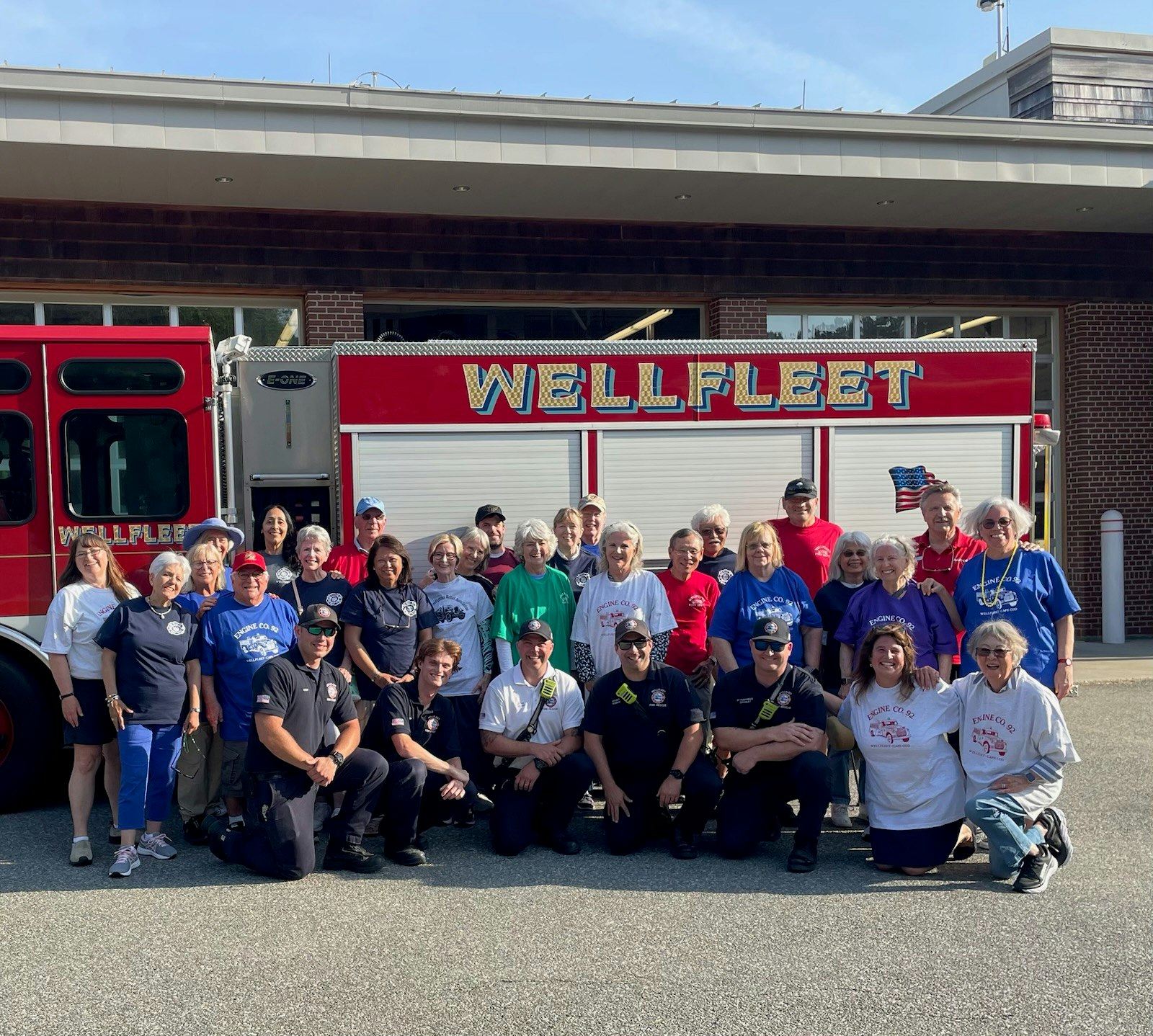 A group of people, including firefighters, pose in front of a "WELLFLEET" fire truck.