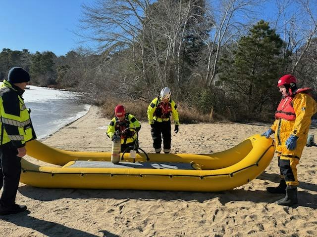 Several people in safety gear handling an inflatable yellow raft on a sandy shoreline.