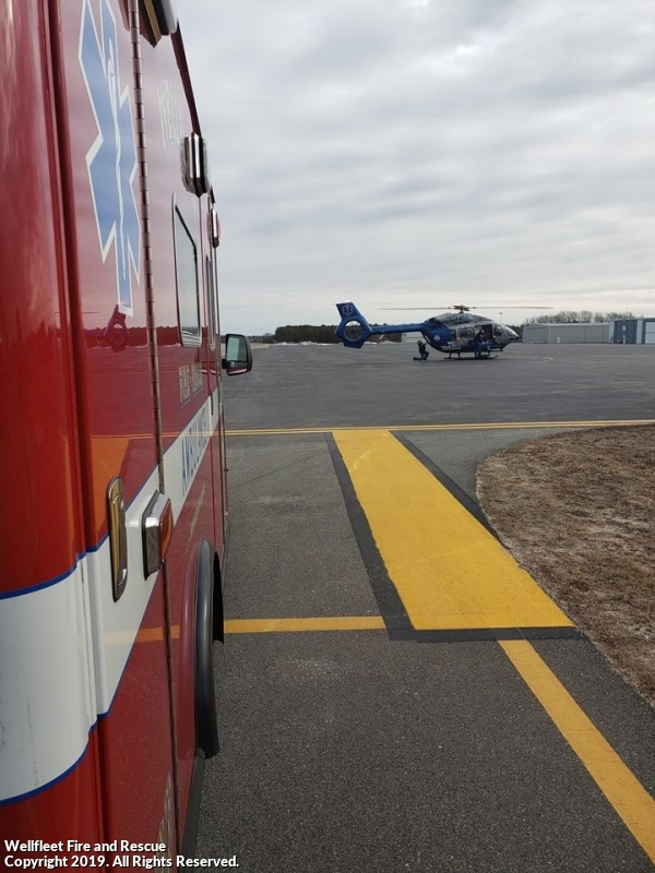 A red fire and rescue vehicle with reflective markings alongside a blue helicopter on an airstrip.
