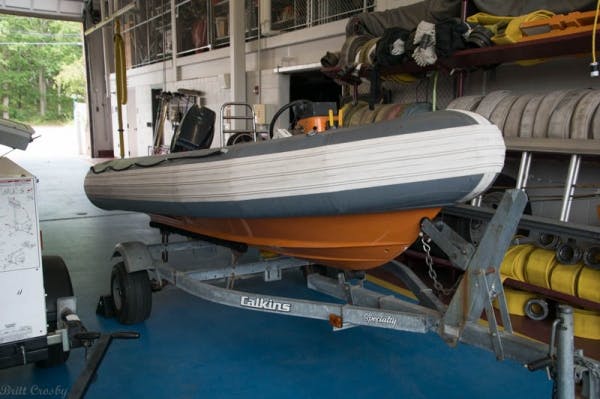 Inflatable boat on a trailer inside a garage with firefighting gear in the background.