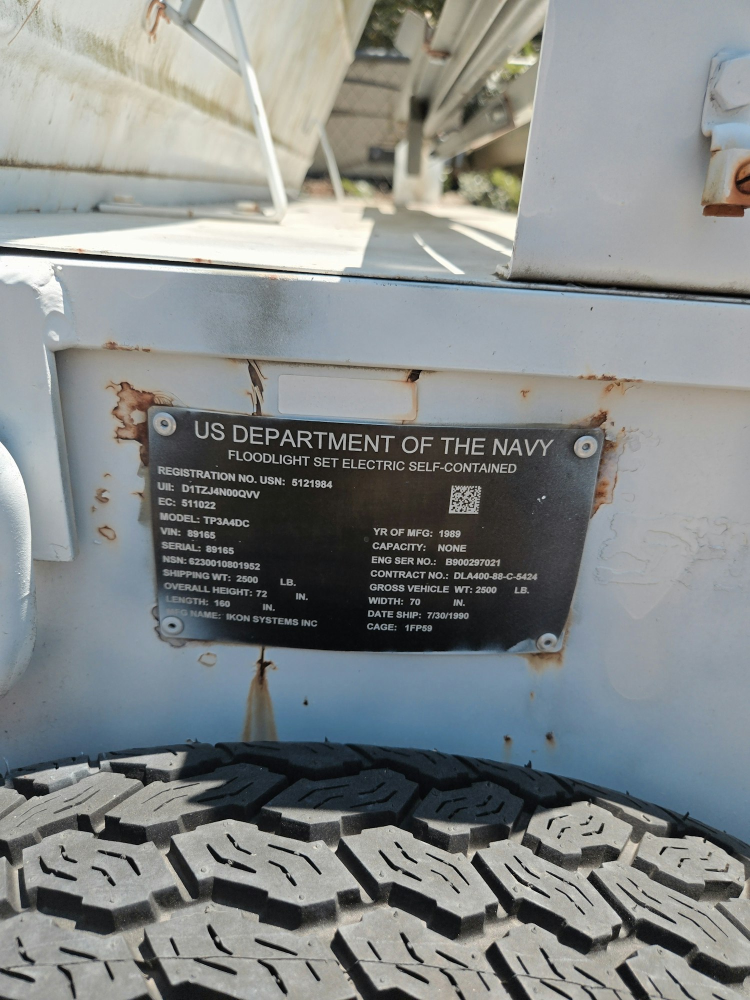 US Navy equipment label on metal near a large tire, detailing a floodlight set.