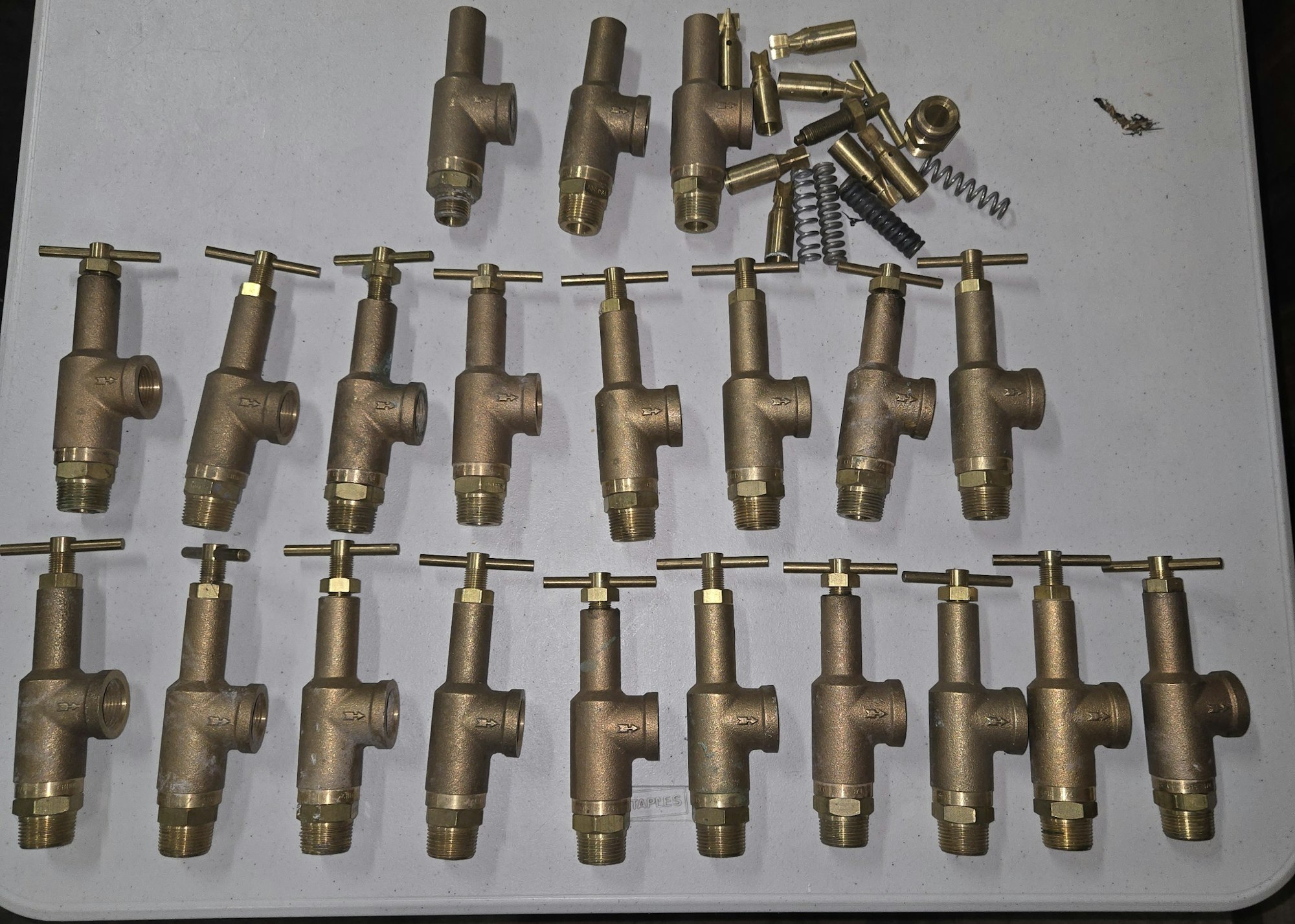 Rows of brass plumbing valves with handles and a few loose components on a table.