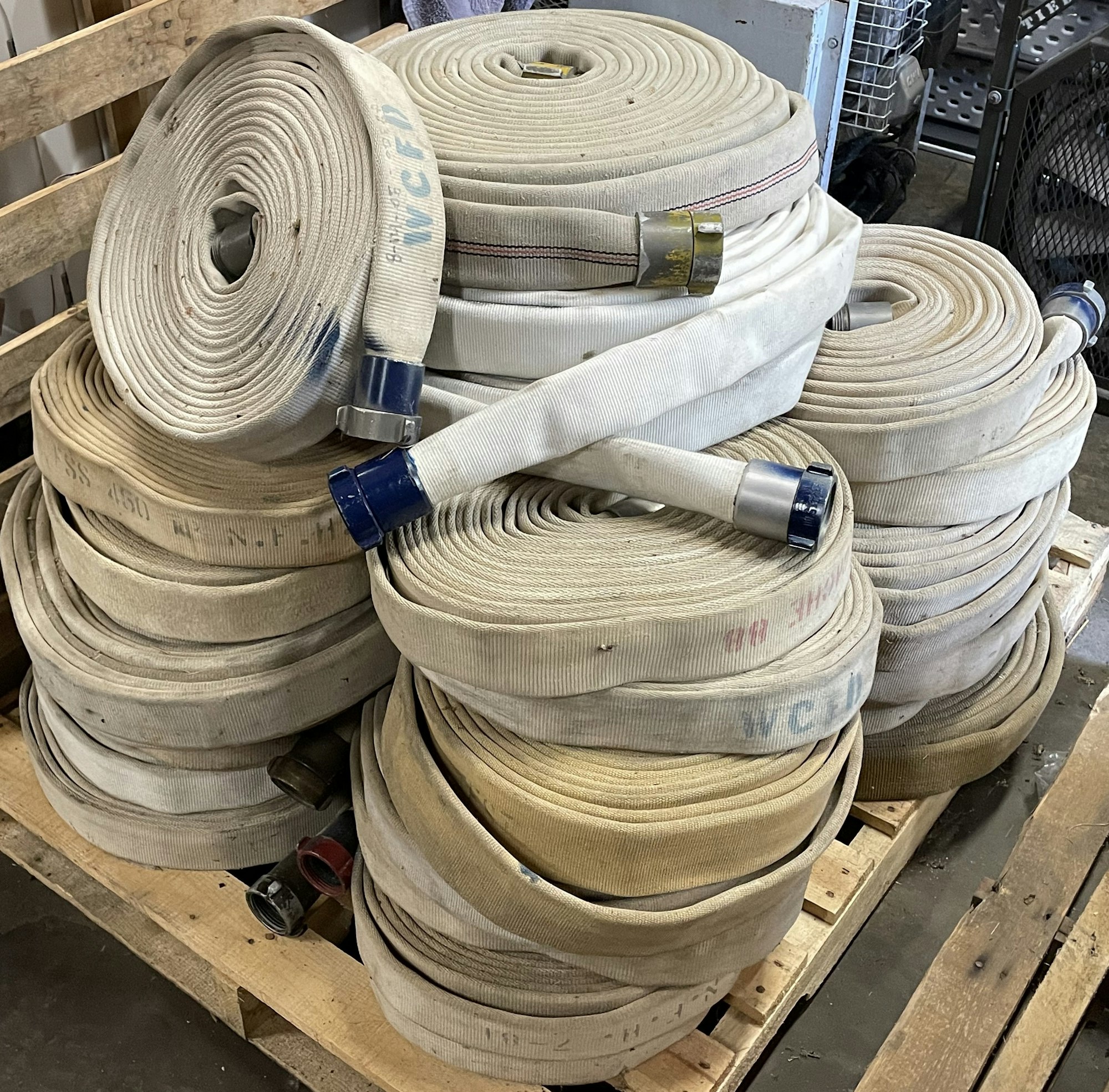 Coiled fire hoses stacked on a wooden pallet in a storage area.