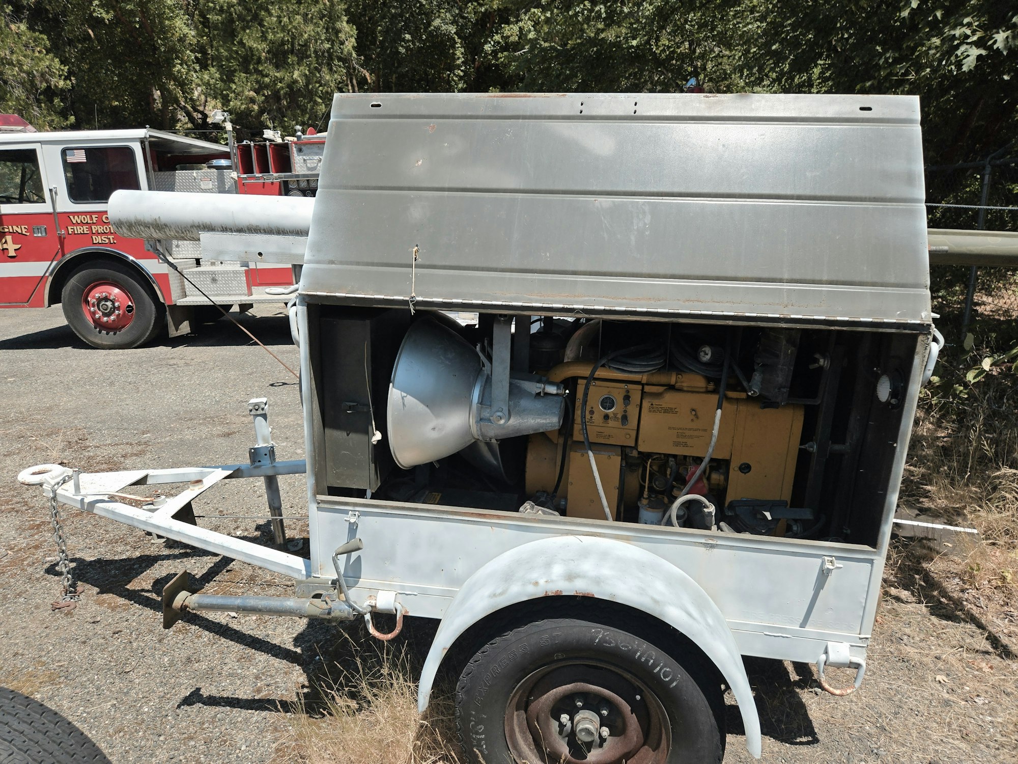 A trailer generator with open side, next to a fire truck in an outdoor area.