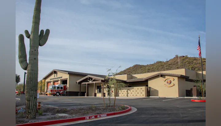 Desert fire station with a fire truck, large cactus, mountain, and an American flag.