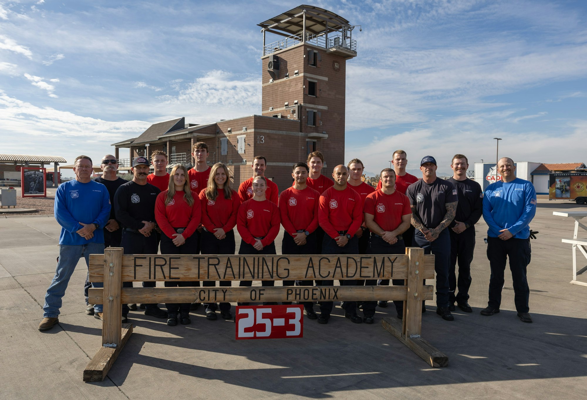 A group of trainees and instructors poses at the Fire Training Academy in Phoenix, in front of a training tower.