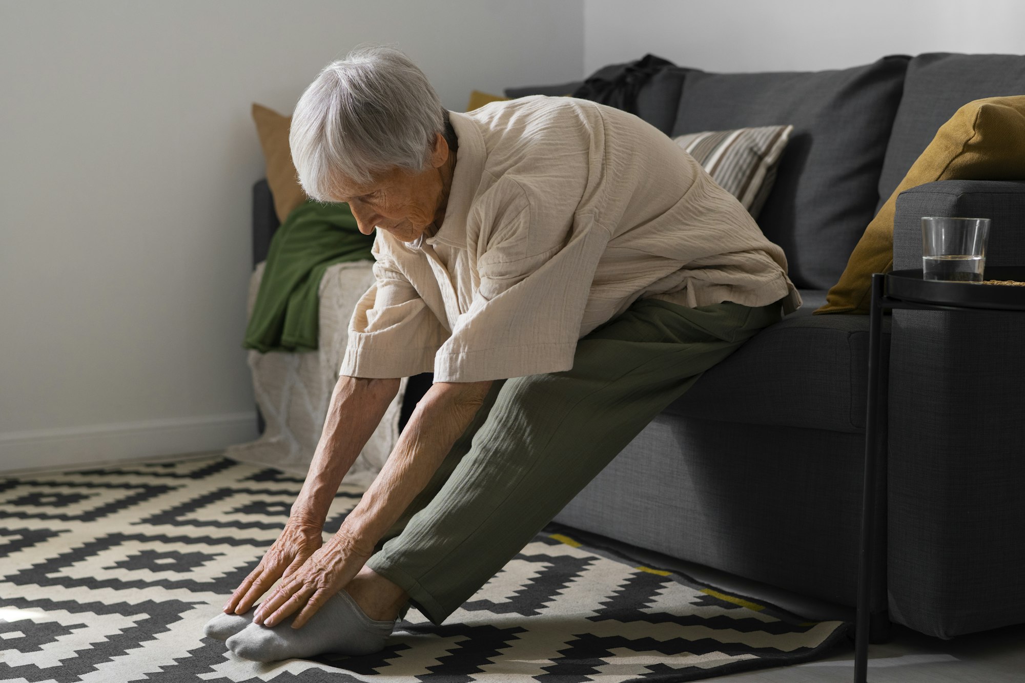 An elderly person stretching on a sofa in a living room.
