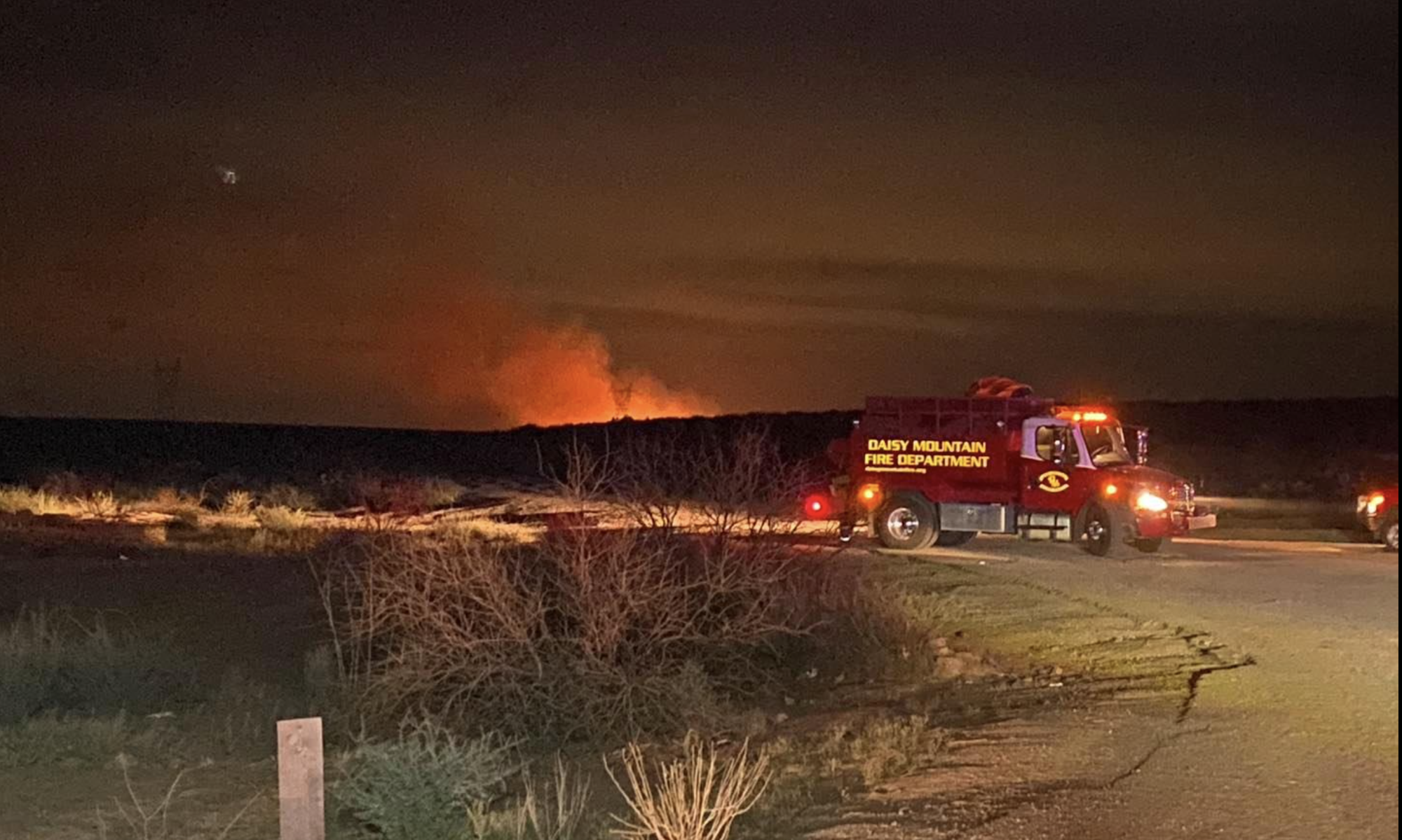 Fire truck at night near a distant blaze, with "Daisy Mountain Fire Department" on the vehicle.