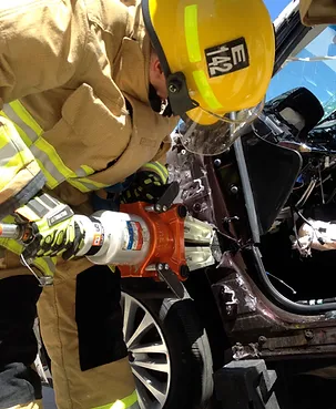 Photo of a firefighter with a tool and a damaged car