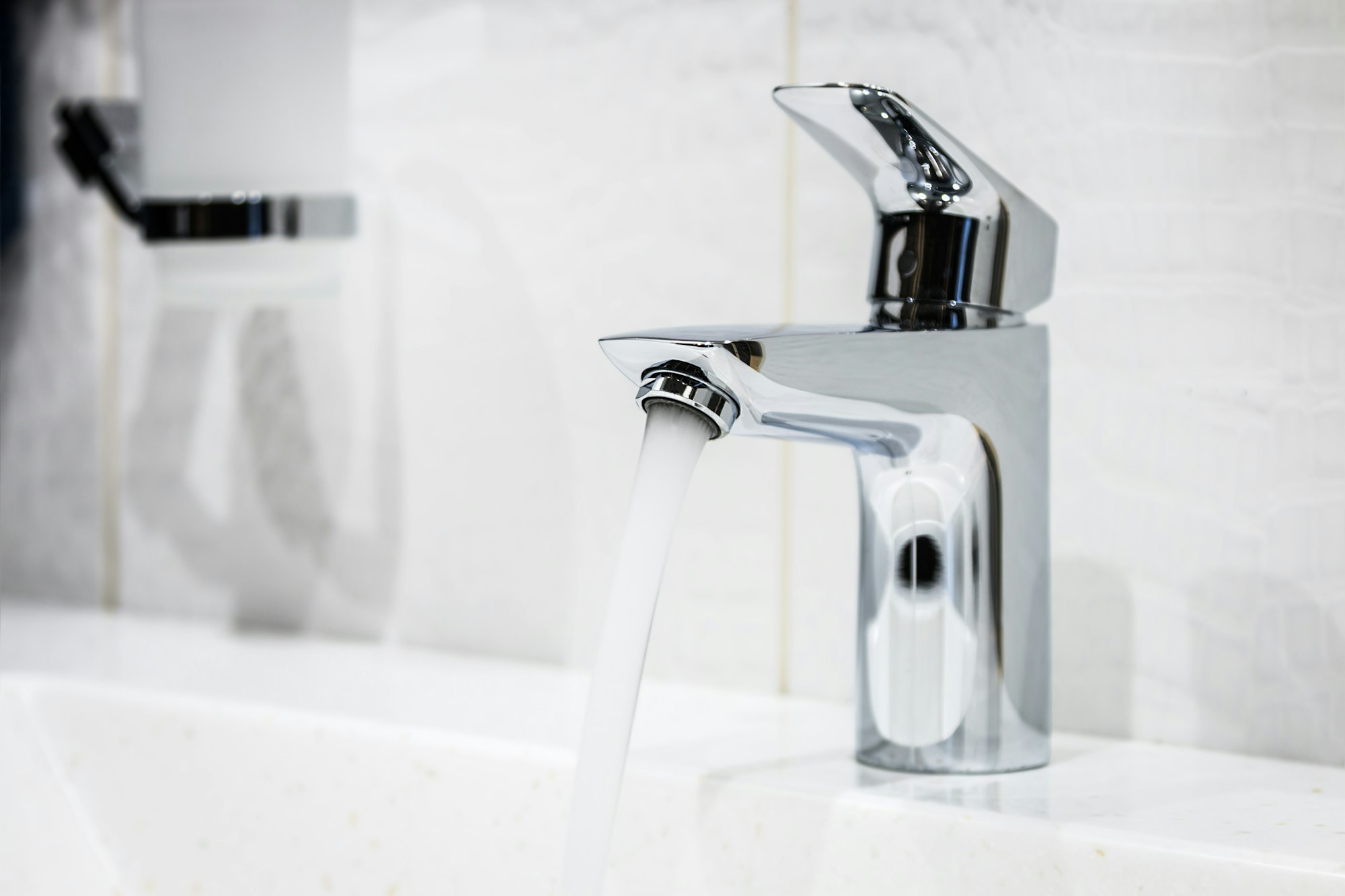 A modern chrome faucet with running water over a white sink.