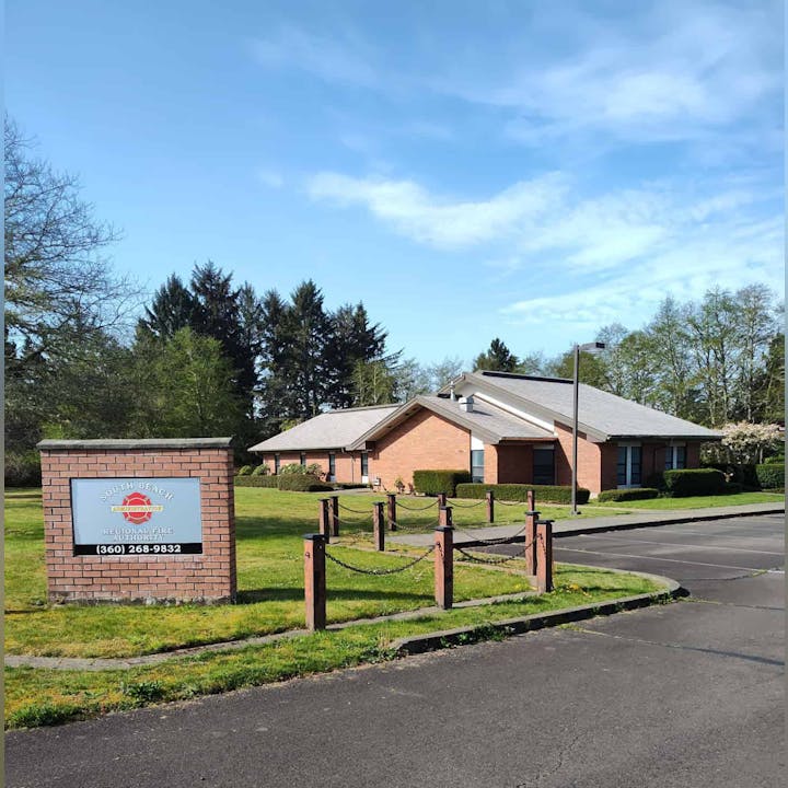 A brick building with a sign reading "South Beach Regional Fire Authority" and a phone number, surrounded by greenery and trees.