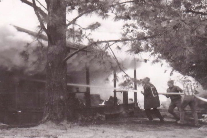 The image depicts firefighters battling a house fire, with smoke billowing from the structure.
