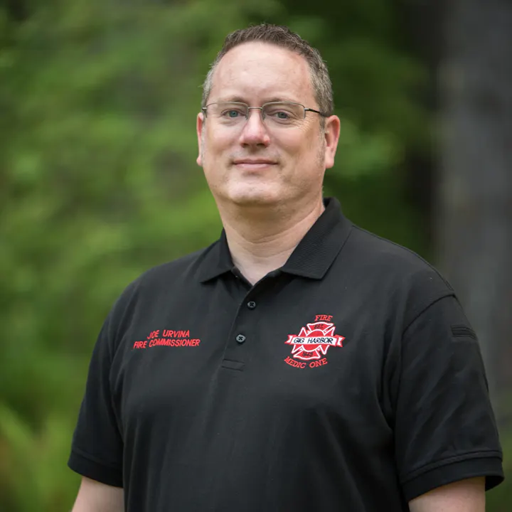 A man in a black polo shirt with "Fire Commissioner" and "Medic One" text, standing outdoors against a blurred green background.