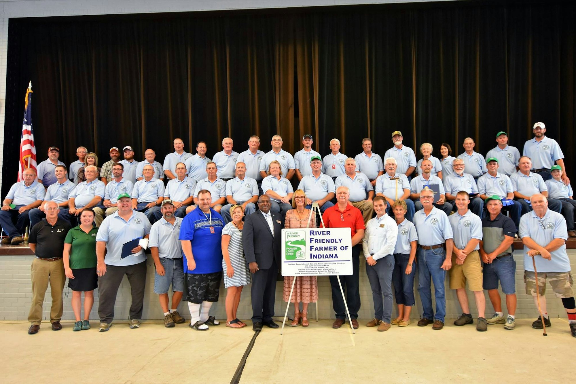 Group photo of people with a "River Friendly Farmer of Indiana" sign, likely recognizing sustainable farming practices.