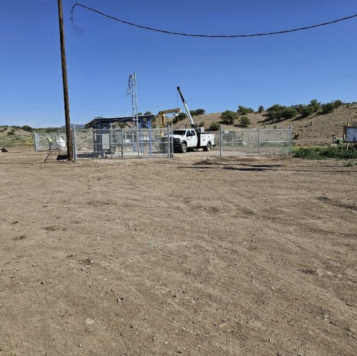 Rural setting with a chain-link fenced area, utility poles, and a white truck with a boom arm.