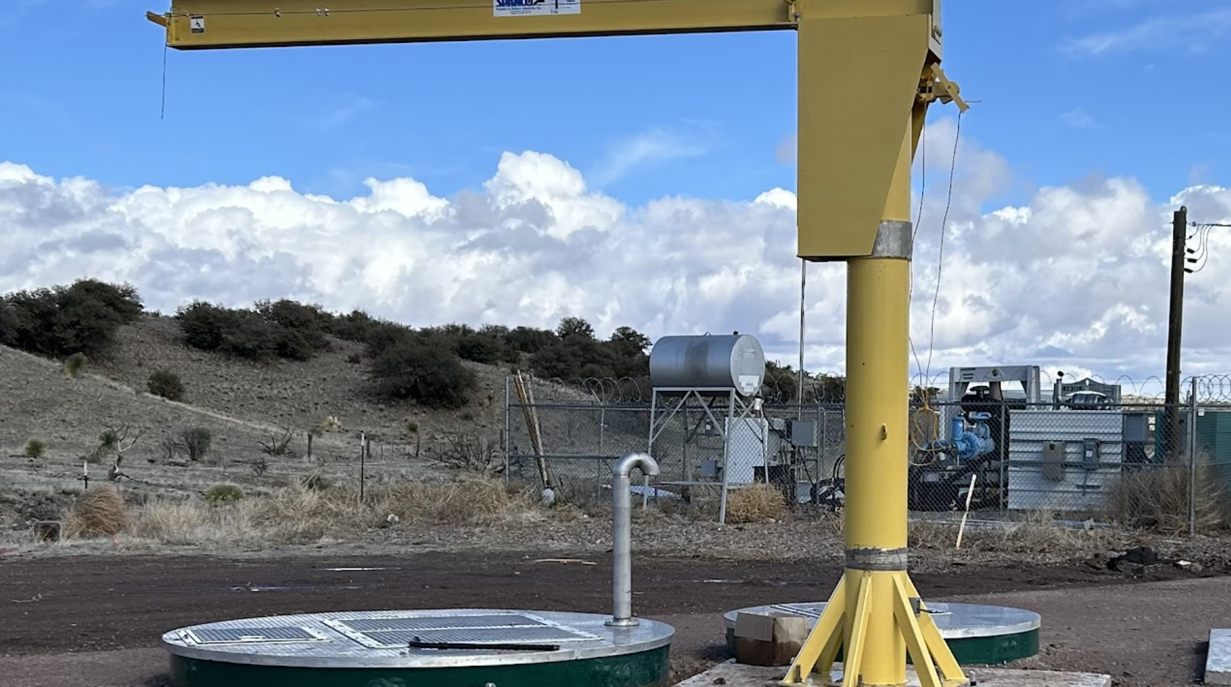 Industrial setting with a crane, tanks, fencing, and cloudy sky.
