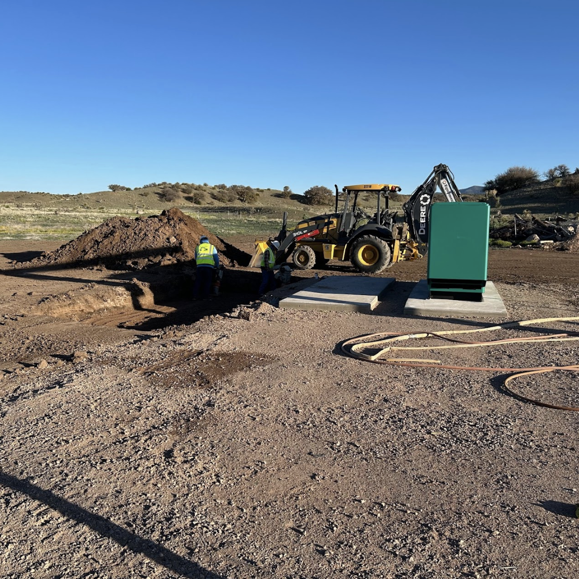 Workers, a backhoe loader, and an electrical cabinet at a construction site.
