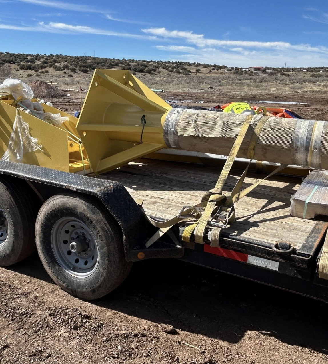 Industrial equipment on a flatbed trailer, secured with straps, under a clear sky.