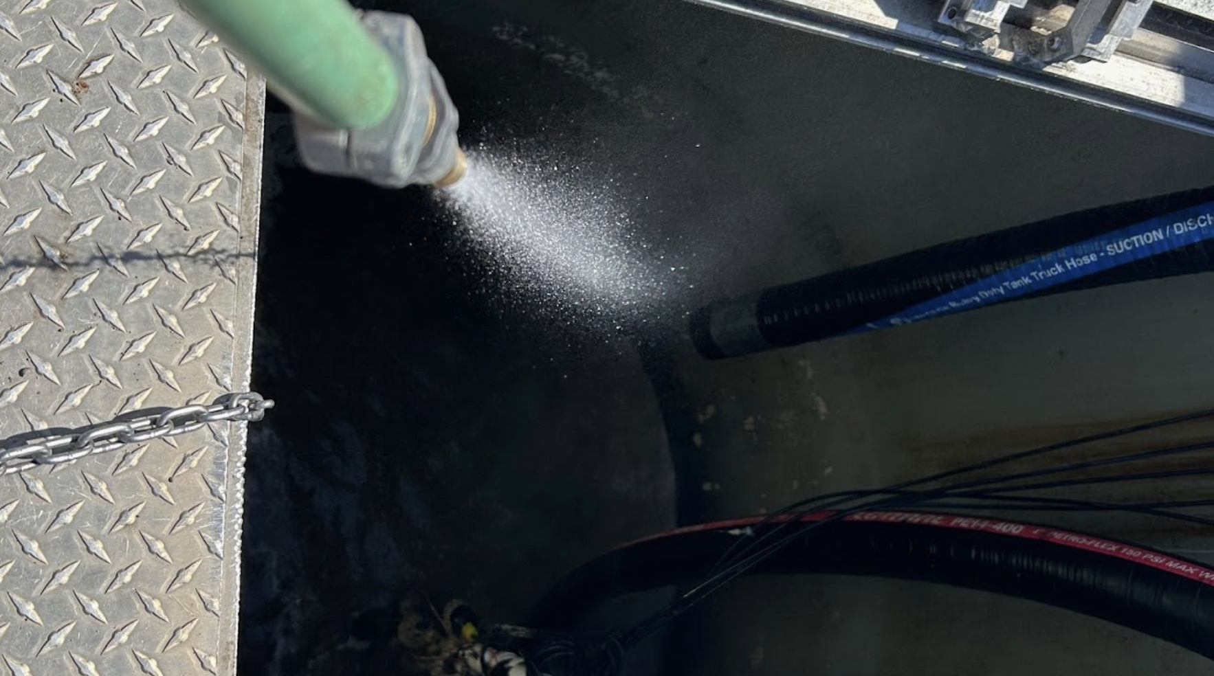 Pressure washing with a high-pressure nozzle, spraying water on a metal surface with hoses visible.