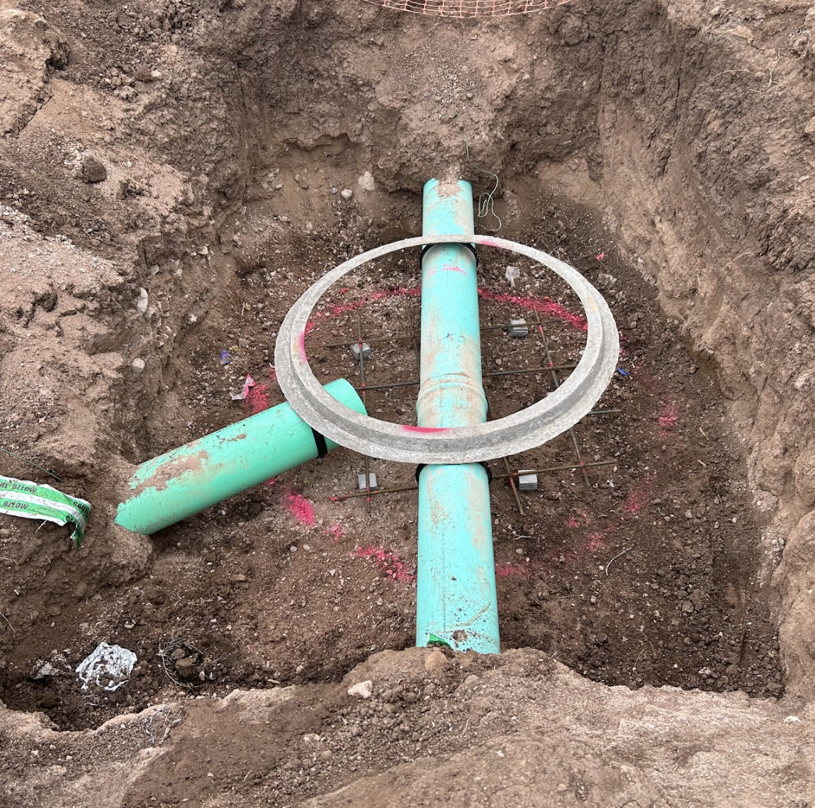 Underground pipes with a circular reinforcement cage, possibly for construction, viewed from above in a dug pit.
