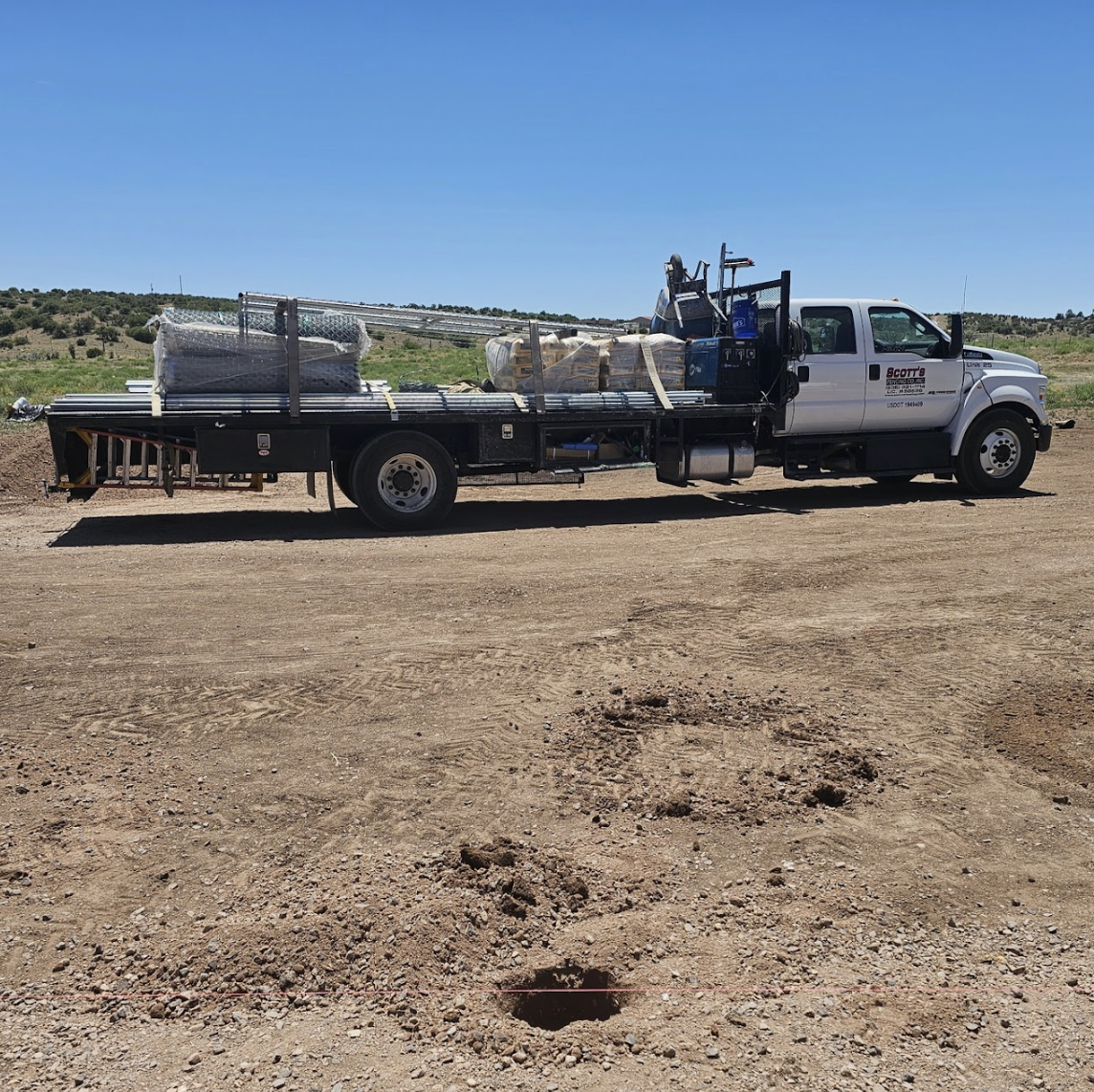A flatbed truck loaded with construction supplies, parked on a dirt surface under a clear sky.