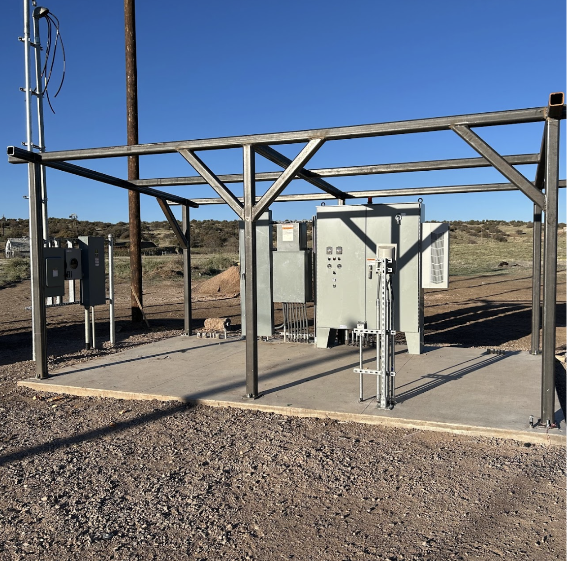 Electrical equipment including control boxes and metallic framework, possibly part of an energy distribution installation, under a clear sky.