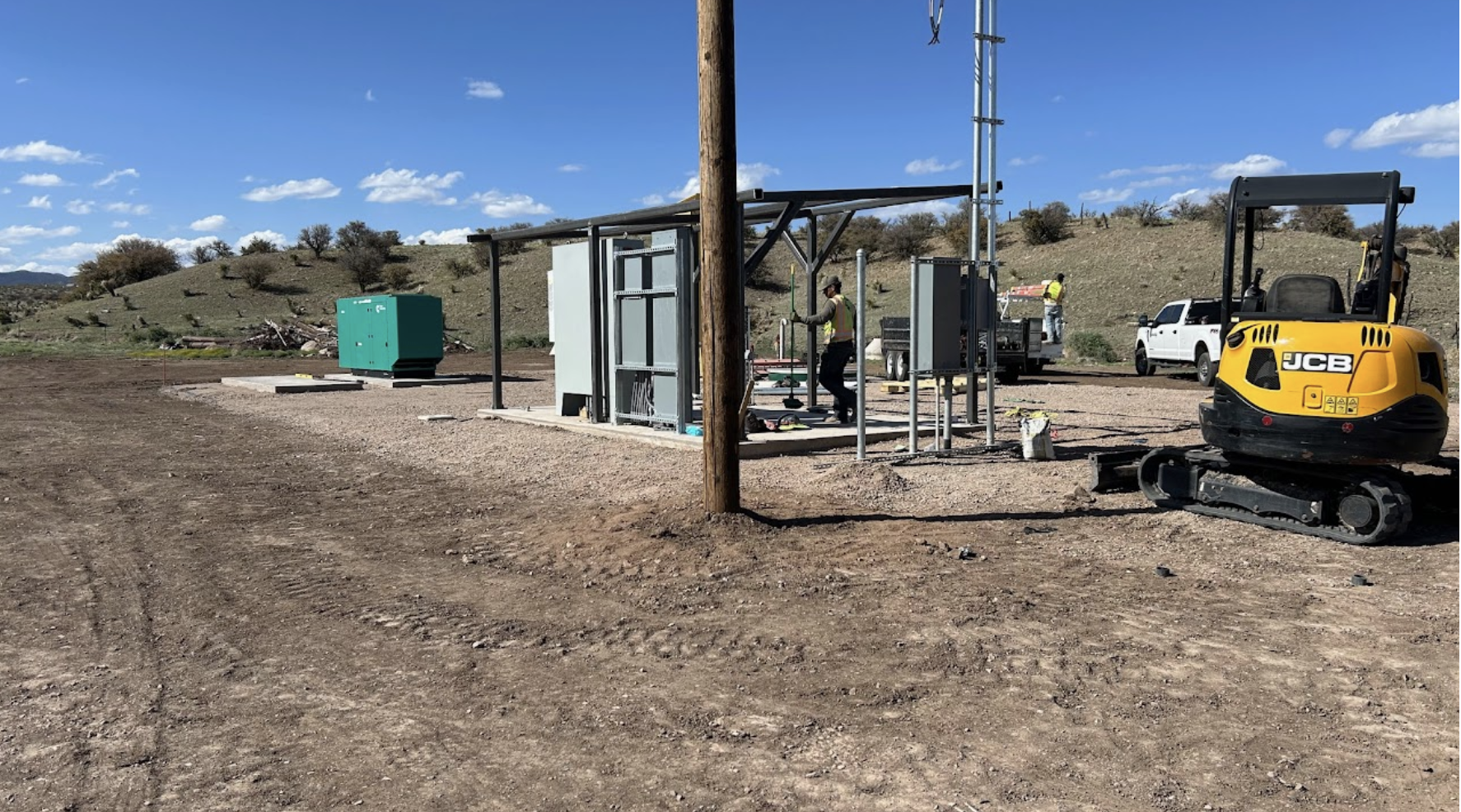 Industrial site with workers, electrical equipment, a generator, and construction machinery on a sunny day.