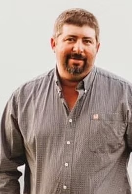 A man with a beard and a mustache wearing a button-up shirt.