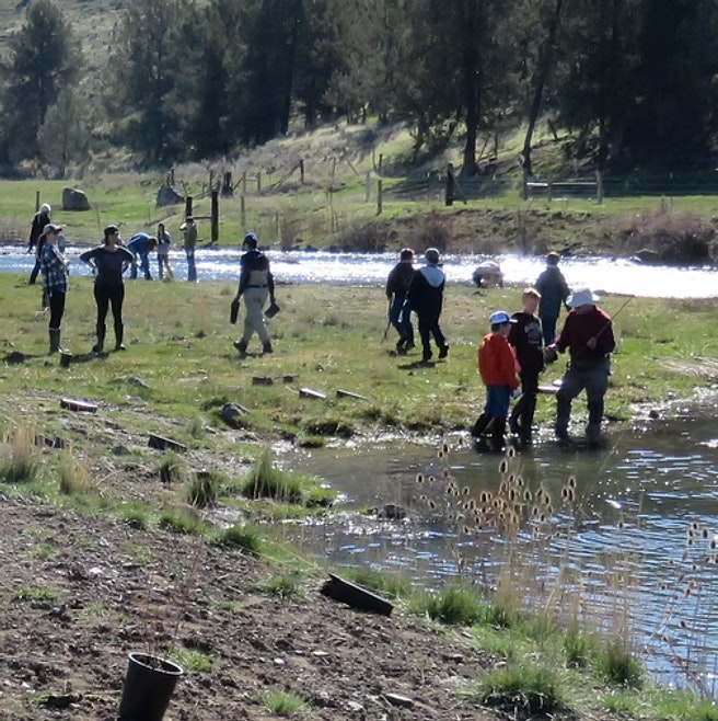 People working together by a river, possibly involved in a restoration or cleanup activity, with some wearing boots or waders.