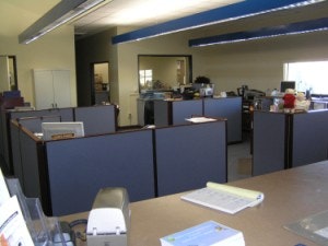 An office space with cubicles, a counter with a notepad, documents, and office equipment.